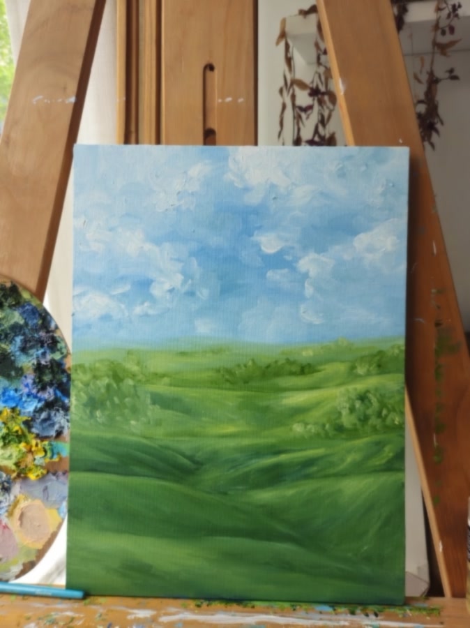 Bright sky: rolling green fields under a big blue sky and thick white clouds, on the easel beside the palette