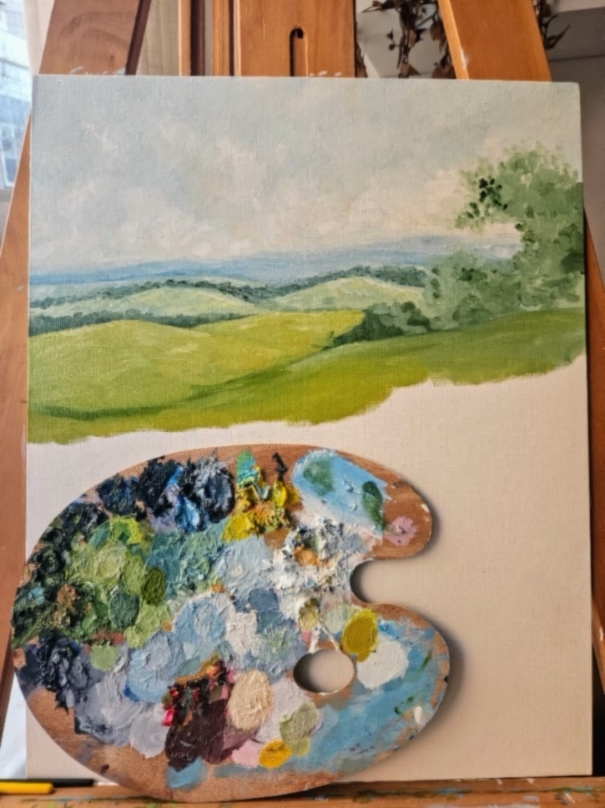Hills, in progress: layered green hills fading to blue and a leafy tree on the right, with a well-used palette propped in front